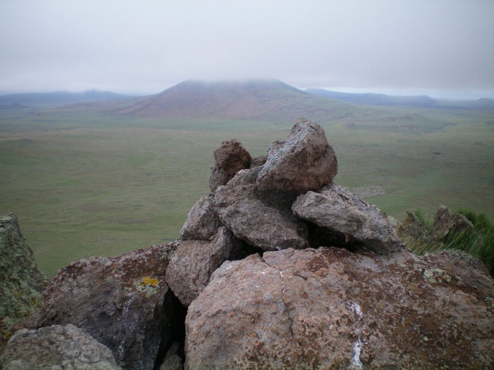 The newly-built summit cairn atop Peak 5273 with cloud-shrouded Wedge Butte in the background. Notice the herd of sheep down on the valley floor (just right of the cairn—look closely). Livingston Douglas Photo